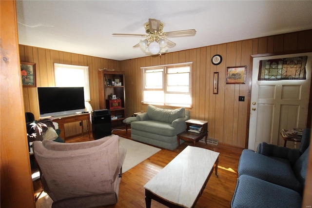 living room with light wood-type flooring, wood walls, and ceiling fan