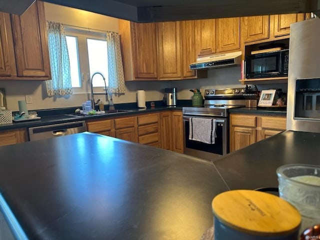 kitchen featuring dark countertops, under cabinet range hood, appliances with stainless steel finishes, and a sink