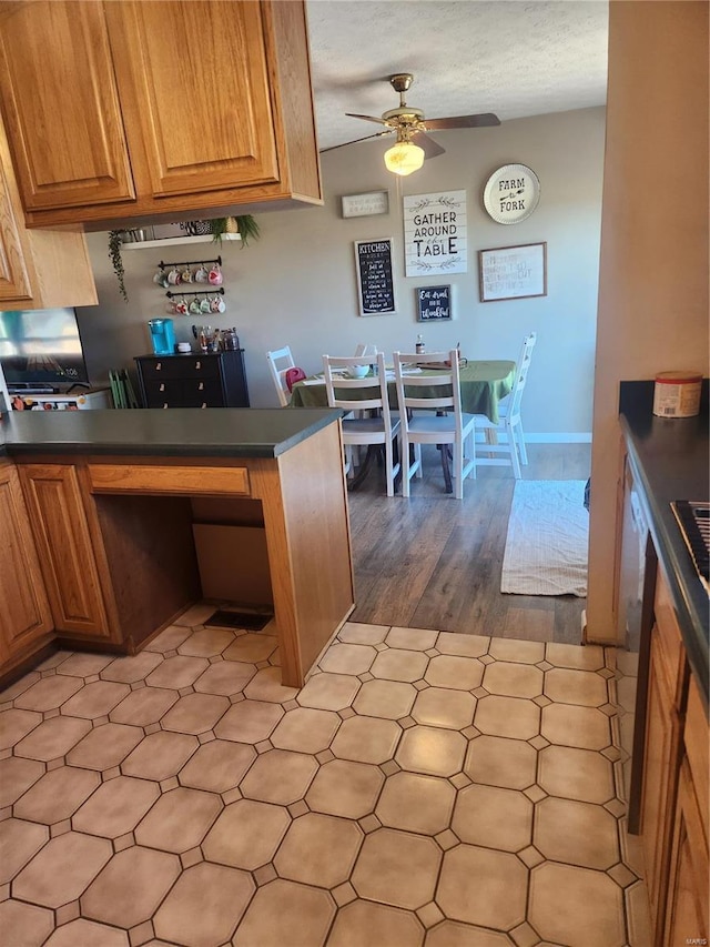 kitchen with dark countertops, ceiling fan, baseboards, and brown cabinetry