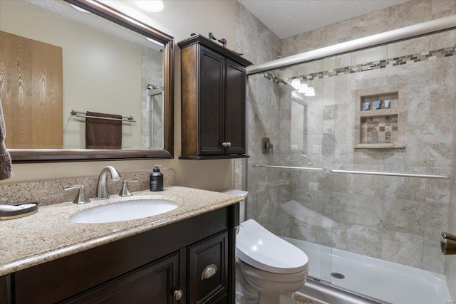 bathroom featuring a textured ceiling, vanity, toilet, and a shower with door