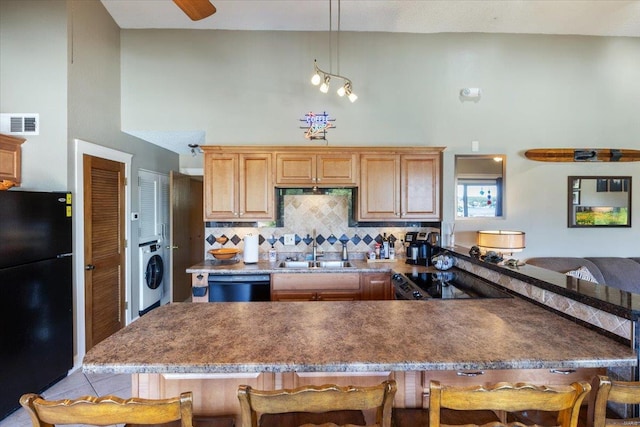 kitchen with black appliances, a kitchen bar, sink, and washer / dryer