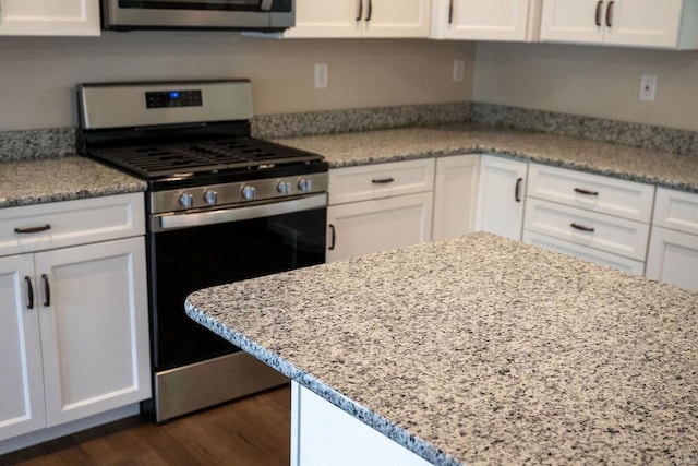 kitchen with stainless steel gas range oven, dark wood-type flooring, light stone counters, and white cabinetry