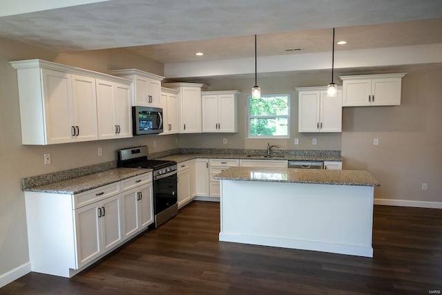 kitchen with appliances with stainless steel finishes, hanging light fixtures, white cabinetry, and a kitchen island