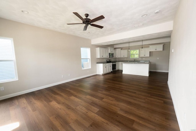 unfurnished living room featuring ceiling fan, a healthy amount of sunlight, and dark hardwood / wood-style flooring