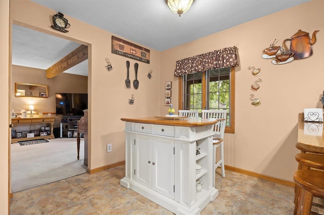 kitchen with white cabinets, beam ceiling, butcher block counters, and light colored carpet