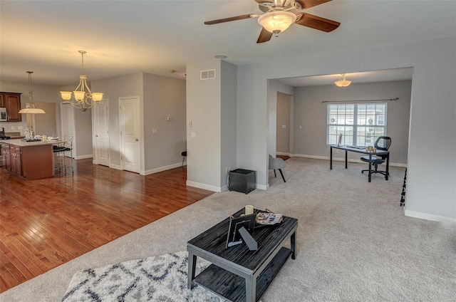 living room featuring ceiling fan with notable chandelier and dark wood-type flooring