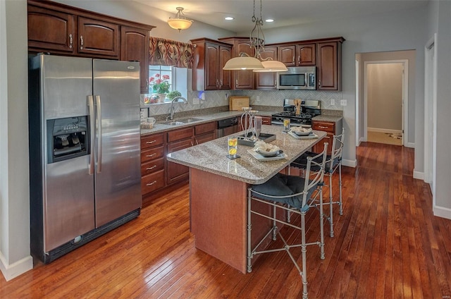 kitchen with light stone countertops, stainless steel appliances, sink, dark hardwood / wood-style floors, and a kitchen island