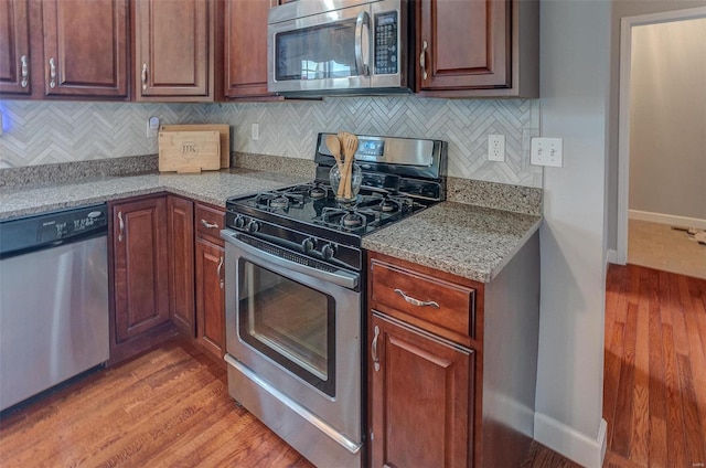 kitchen featuring light stone countertops, backsplash, stainless steel appliances, and light hardwood / wood-style flooring