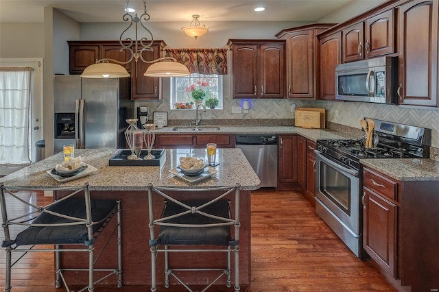 kitchen with a kitchen breakfast bar, sink, decorative light fixtures, a kitchen island, and stainless steel appliances