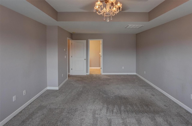 empty room featuring a tray ceiling, carpet floors, and an inviting chandelier