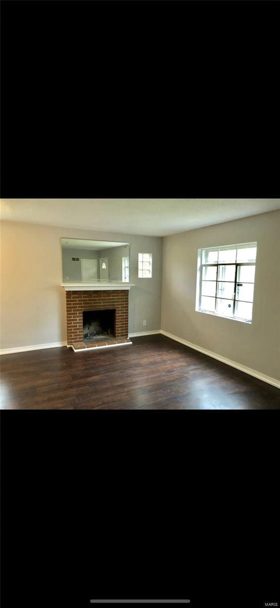 unfurnished living room with dark wood-type flooring and a brick fireplace