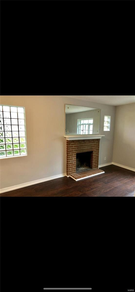 unfurnished living room featuring a brick fireplace and dark hardwood / wood-style floors