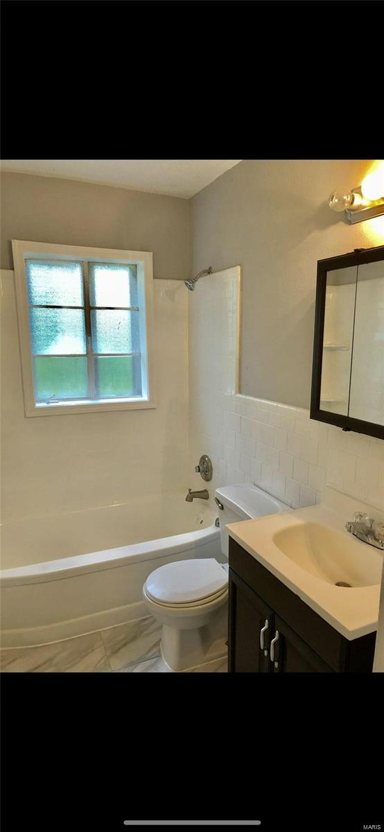 full bathroom with  shower combination, vanity, tile walls, and toilet