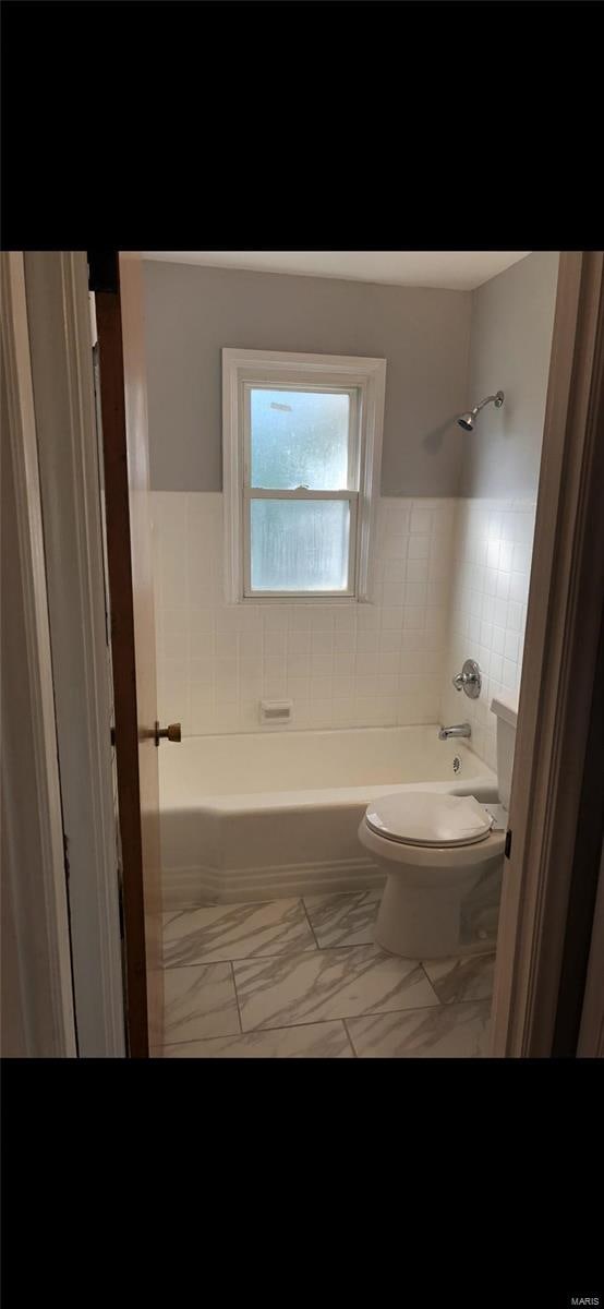 bathroom with tile walls, tiled shower / bath, and toilet