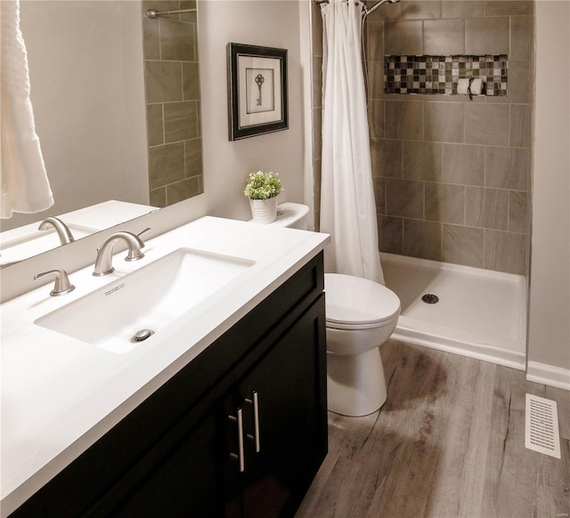 bathroom with hardwood / wood-style flooring, vanity, toilet, and walk in shower