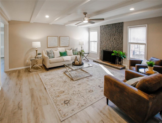 living room with beam ceiling, light wood-type flooring, a stone fireplace, and ceiling fan