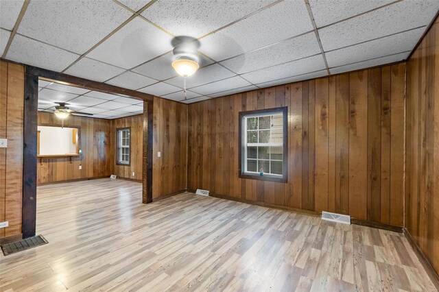 spare room featuring light hardwood / wood-style flooring, wood walls, and a drop ceiling