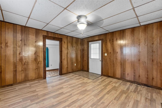 empty room with ceiling fan, wooden walls, light hardwood / wood-style flooring, and a paneled ceiling