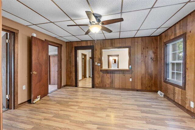 unfurnished room featuring ceiling fan, wooden walls, light wood-type flooring, and a paneled ceiling