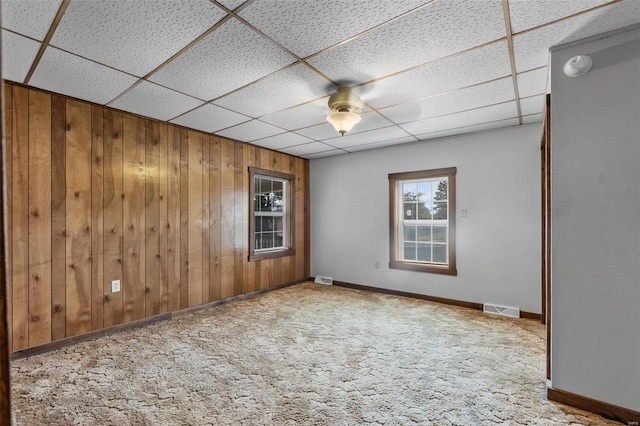 unfurnished room with wooden walls, a drop ceiling, and carpet