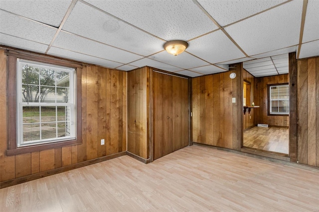 unfurnished room featuring a drop ceiling, wood walls, and light hardwood / wood-style flooring