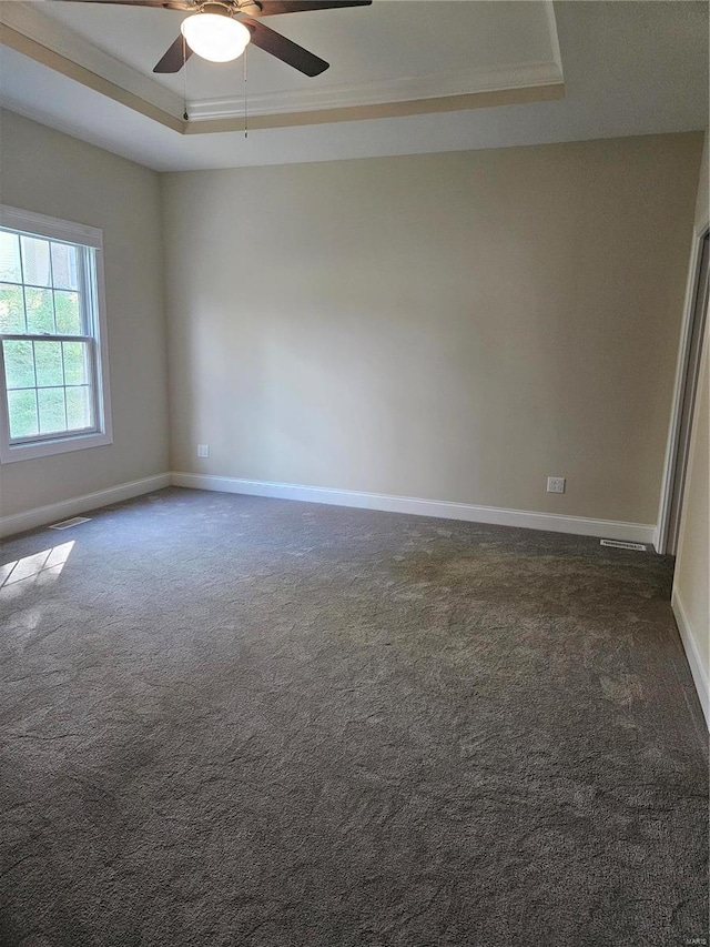 spare room featuring dark carpet, ceiling fan, a raised ceiling, and crown molding