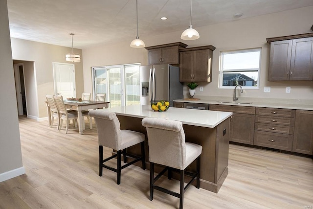 kitchen with sink, light hardwood / wood-style flooring, stainless steel fridge, pendant lighting, and a kitchen island