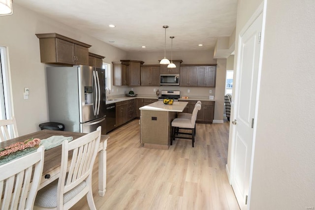 kitchen with sink, a center island, hanging light fixtures, light hardwood / wood-style floors, and appliances with stainless steel finishes