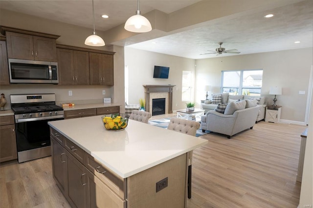 kitchen with a center island, hanging light fixtures, a breakfast bar area, appliances with stainless steel finishes, and light wood-type flooring