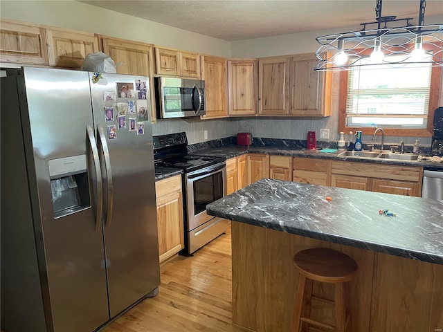 kitchen with hanging light fixtures, sink, a kitchen island, stainless steel appliances, and light wood-type flooring