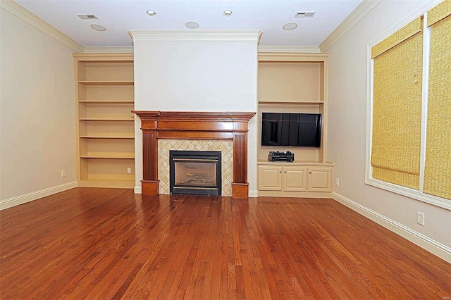 unfurnished living room featuring crown molding, a tiled fireplace, hardwood / wood-style flooring, and built in features