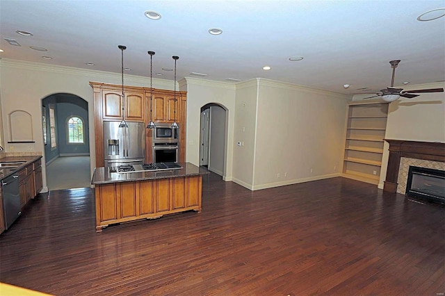 kitchen featuring appliances with stainless steel finishes, a tiled fireplace, decorative light fixtures, dark wood-type flooring, and ornamental molding