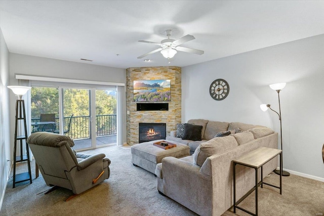 carpeted living room featuring a stone fireplace and ceiling fan