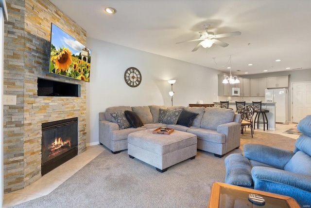 living room with ceiling fan with notable chandelier, light colored carpet, and a stone fireplace