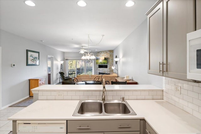 kitchen featuring gray cabinetry, a stone fireplace, white appliances, light tile patterned floors, and sink