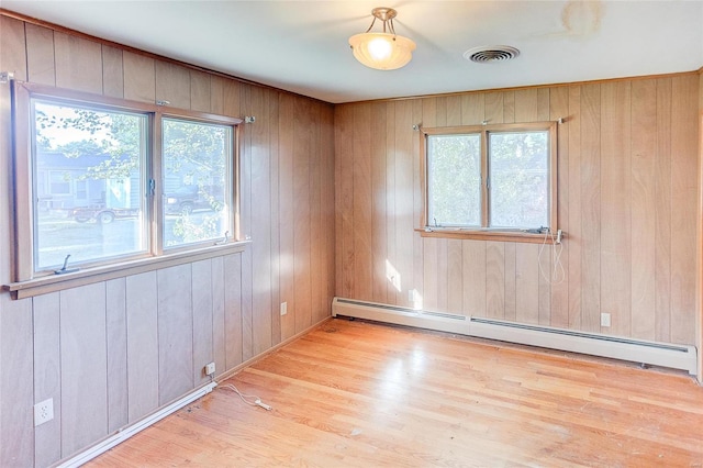 spare room featuring baseboard heating, plenty of natural light, wood walls, and light hardwood / wood-style flooring