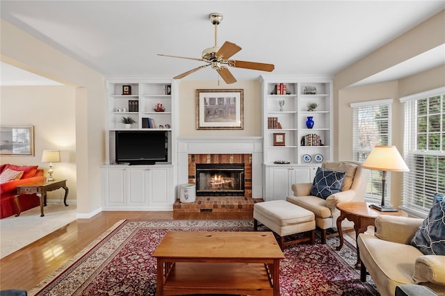 living room with hardwood / wood-style flooring, ceiling fan, a fireplace, and built in shelves