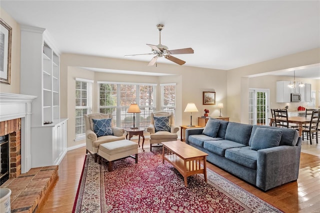 living room featuring hardwood / wood-style flooring, ceiling fan with notable chandelier, and a brick fireplace