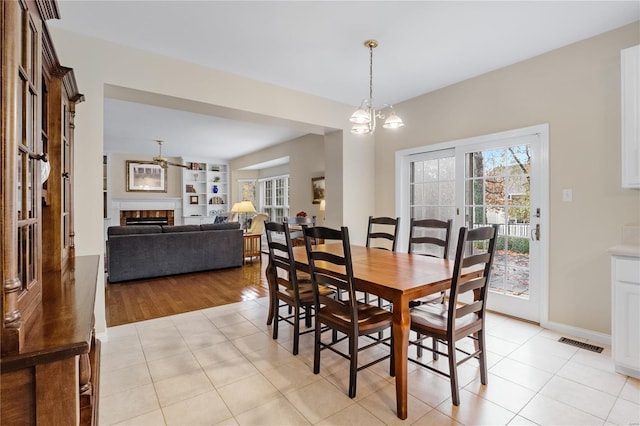 tiled dining room featuring an inviting chandelier, built in shelves, and a fireplace