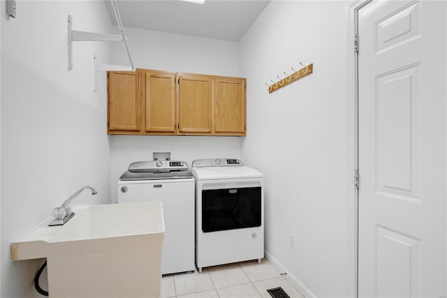 clothes washing area with light tile patterned floors, sink, washer and clothes dryer, and cabinets