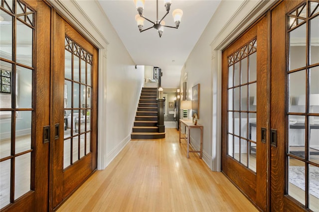 hall with light hardwood / wood-style flooring, french doors, and an inviting chandelier