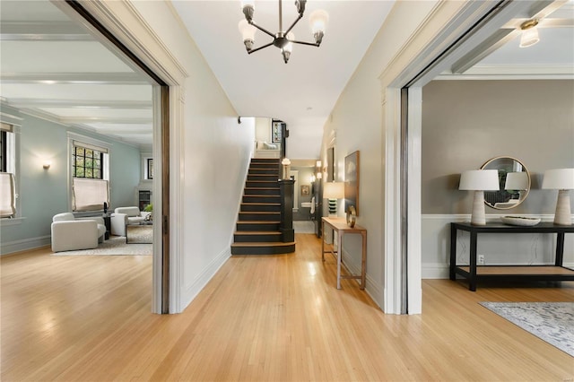 hall featuring light wood-type flooring, ornamental molding, and a notable chandelier