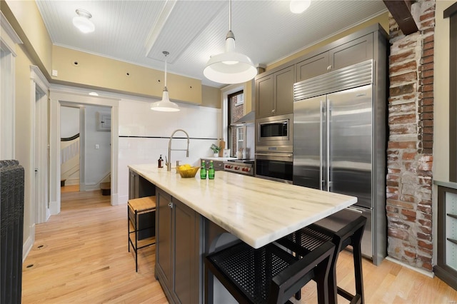 kitchen with built in appliances, light hardwood / wood-style floors, decorative light fixtures, a breakfast bar area, and ornamental molding