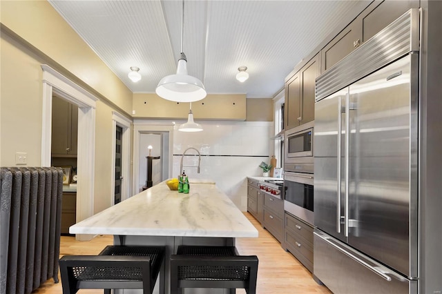 kitchen with light stone countertops, radiator, pendant lighting, built in appliances, and light hardwood / wood-style flooring