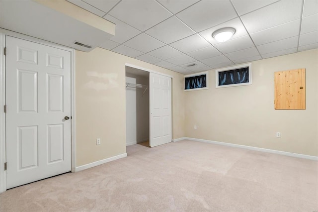 unfurnished bedroom with a closet, light colored carpet, and a paneled ceiling