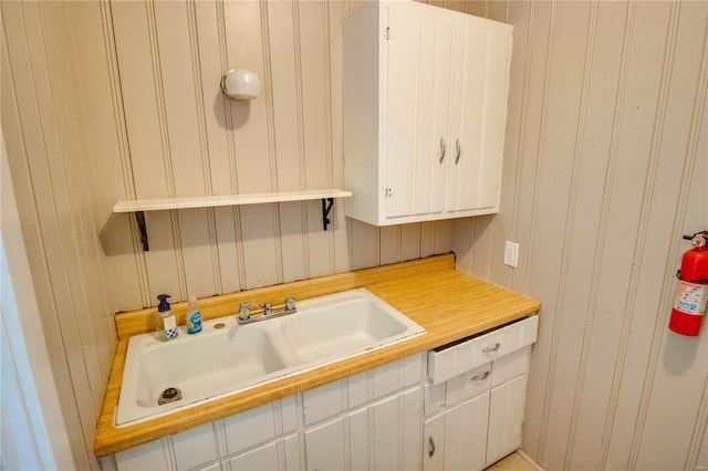 kitchen featuring wood walls, sink, and white cabinetry