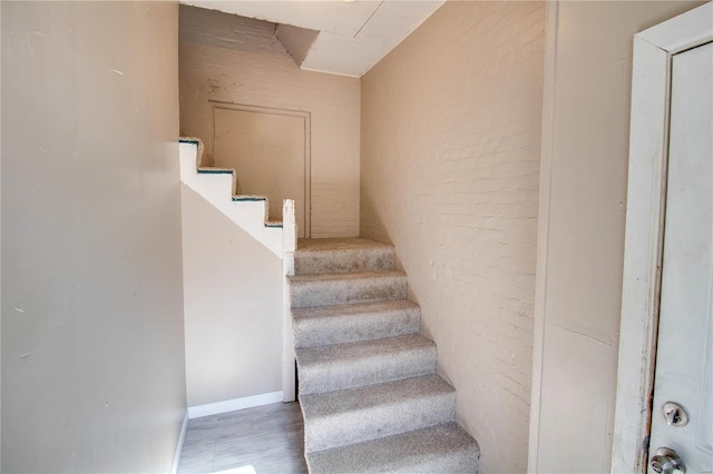 stairs with brick wall and hardwood / wood-style floors