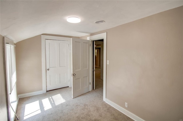 unfurnished bedroom featuring light carpet, lofted ceiling, and multiple windows