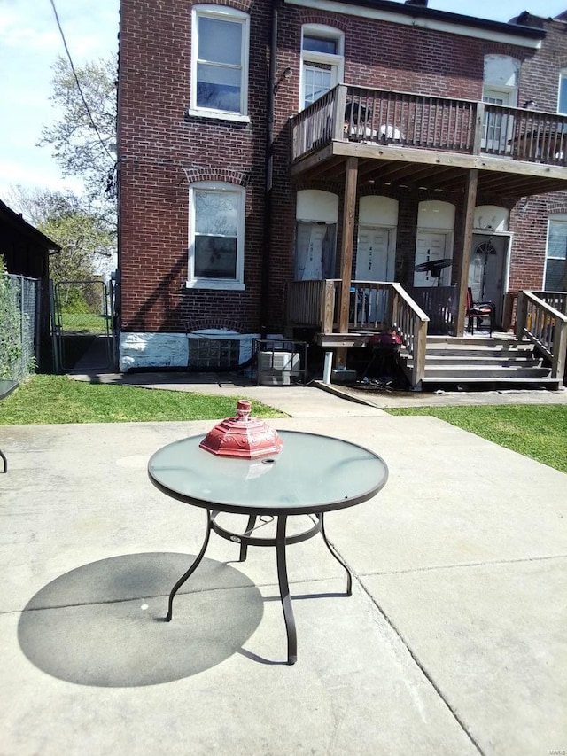 rear view of property featuring brick siding, fence, a patio, and a gate