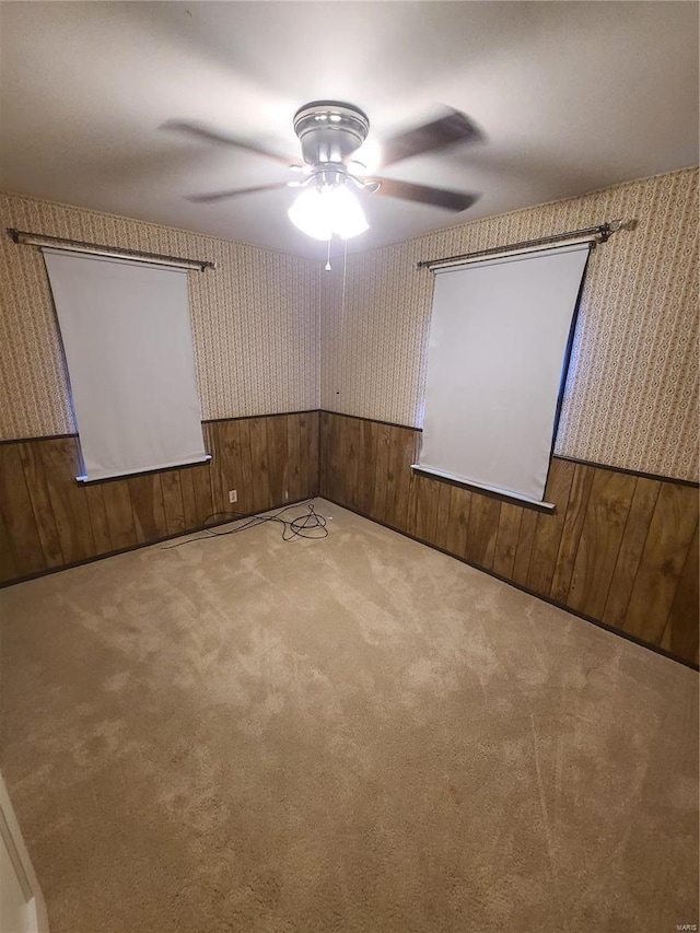 carpeted home theater room with ceiling fan and wood walls